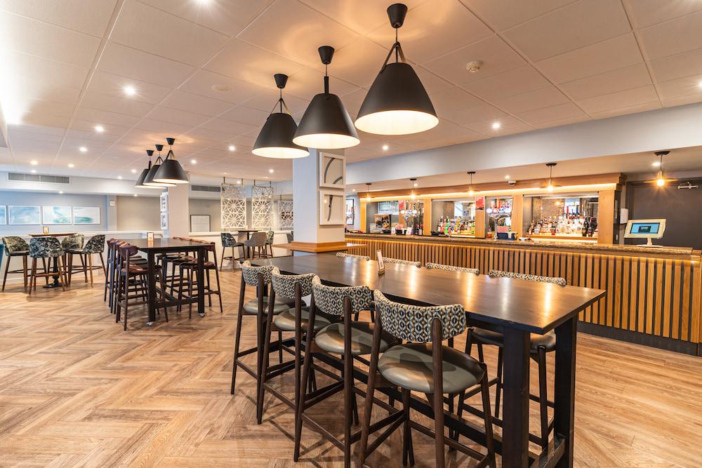 Bar area with tables, high bar chairs, and large black lamps overhead.