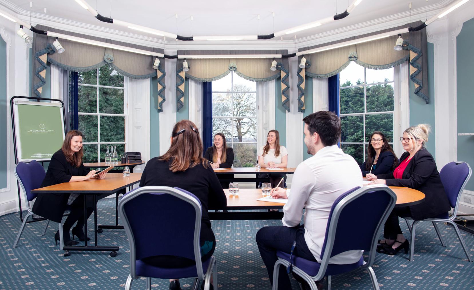 Conference room with people smiling, sitting in rounded arrangements, and taking notes.