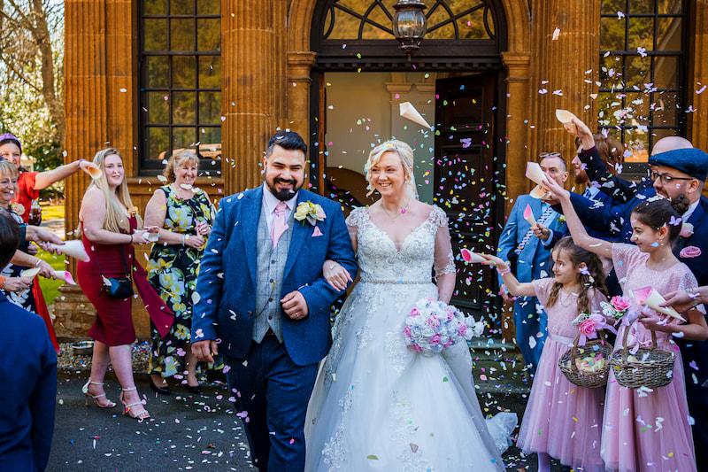 Happy couple and their guests throwing flower petals in celebration.